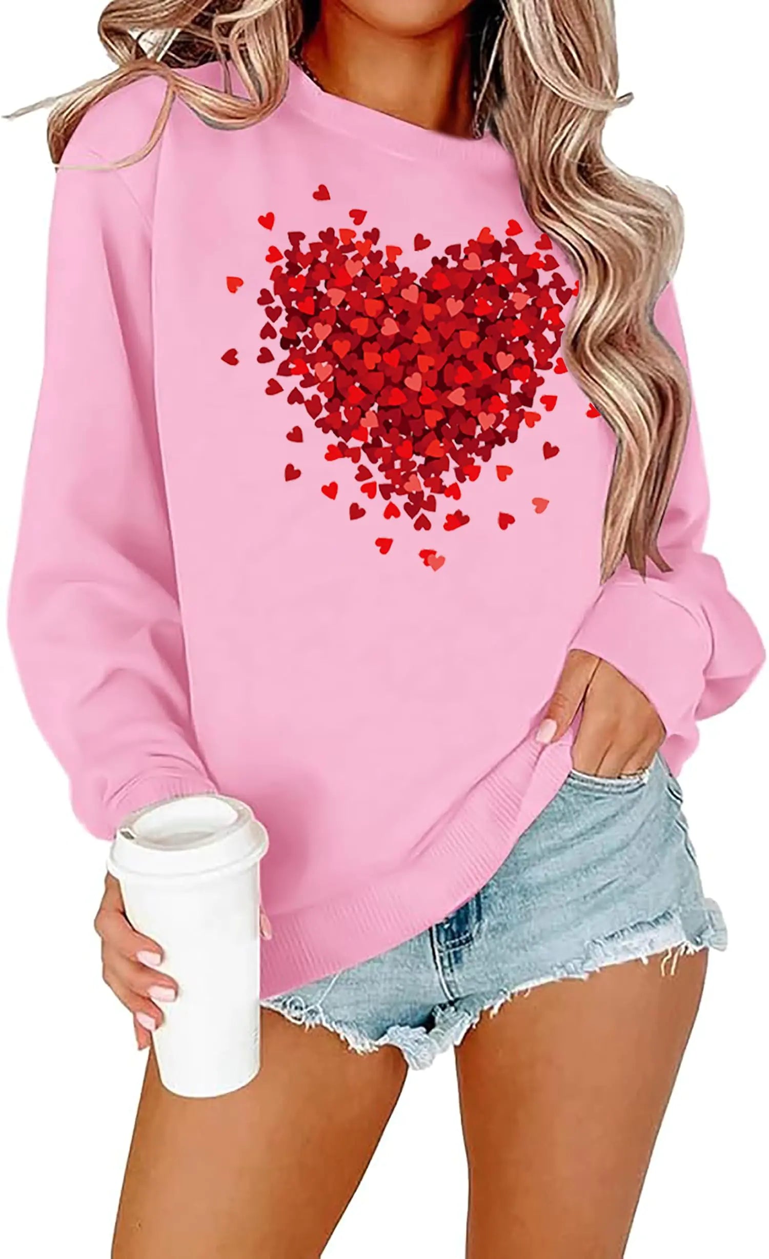 Person wearing a pink sweatshirt with a red heart design, holding a white cup. Women Valentines Apparel.