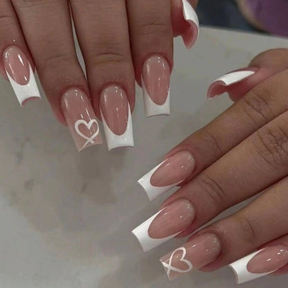 Close-up of hands with long, almond-shaped nails featuring a white heart design on a neutral background.